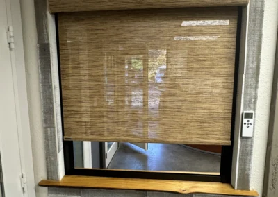 A partially closed bamboo shade in a rustic window frame with a wooden sill, showcasing a minimalist interior design.