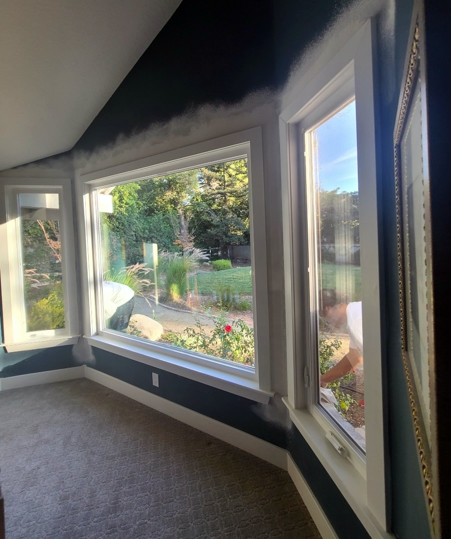 Interior view of newly installed white vinyl windows overlooking a backyard garden.