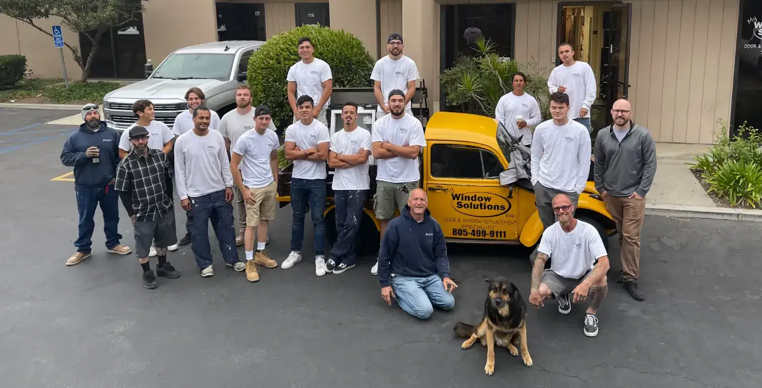 the-crew-and-max-team (1) Team photo of My Window Solutions staff posing outside their office with a branded yellow truck and their company dog